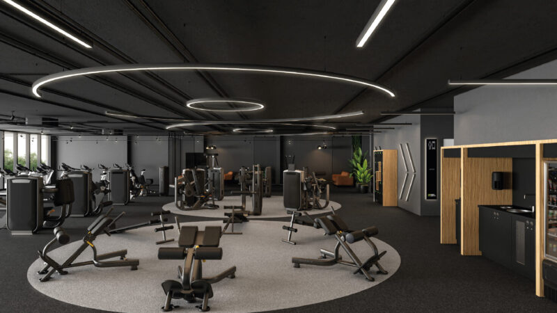 Modernes Fitnessstudio-Franchise mit verschiedenen Trainingsgeräten und Bänken in einem geräumigen, gut beleuchteten Raum mit dunklem Boden, kreisförmiger Deckenbeleuchtung und einem Erfrischungsbereich auf der rechten Seite.
