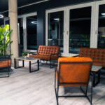 Moderner Loungebereich mit braunen Ledersesseln und Sofas, Holztischen, großen grünen Topfpflanzen und raumhohen Fenstern. Heller, sauberer Raum mit hellem Holzboden und schwarzen Akzenten. Moderner Loungebereich mit braunen Ledersesseln und Sofas, Holztischen, großen grünen Topfpflanzen und raumhohen Fenstern. Heller, sauberer Raum mit hellem Holzboden und schwarzen Akzenten.