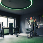 Ein modernes Fitnessstudio mit verschiedenen Trainingsgeräten, großen Fenstern, die viel Tageslicht hereinlassen, und einem Wandposter mit zwei lächelnden Menschen und den Worten „FAMILY“ und „EASY FITNESS“. Der Raum ist sauber und gut beleuchtet. Ein modernes Fitnessstudio mit verschiedenen Trainingsgeräten, großen Fenstern, die viel Tageslicht hereinlassen, und einem Wandposter mit zwei lächelnden Menschen und den Worten „FAMILY“ und „EASY FITNESS“. Der Raum ist sauber und gut beleuchtet.
