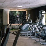 Ein modernes Fitnessstudio mit mehreren Laufbändern und Trainingsgeräten. An der Wand hängt ein großes Foto einer Person, die im Wald joggt. Das Fitnessstudio ist gut beleuchtet – sowohl mit natürlichem als auch mit künstlichem Licht. Ein modernes Fitnessstudio mit mehreren Laufbändern und Trainingsgeräten. An der Wand hängt ein großes Foto einer Person, die im Wald joggt. Das Fitnessstudio ist gut beleuchtet – sowohl mit natürlichem als auch mit künstlichem Licht.